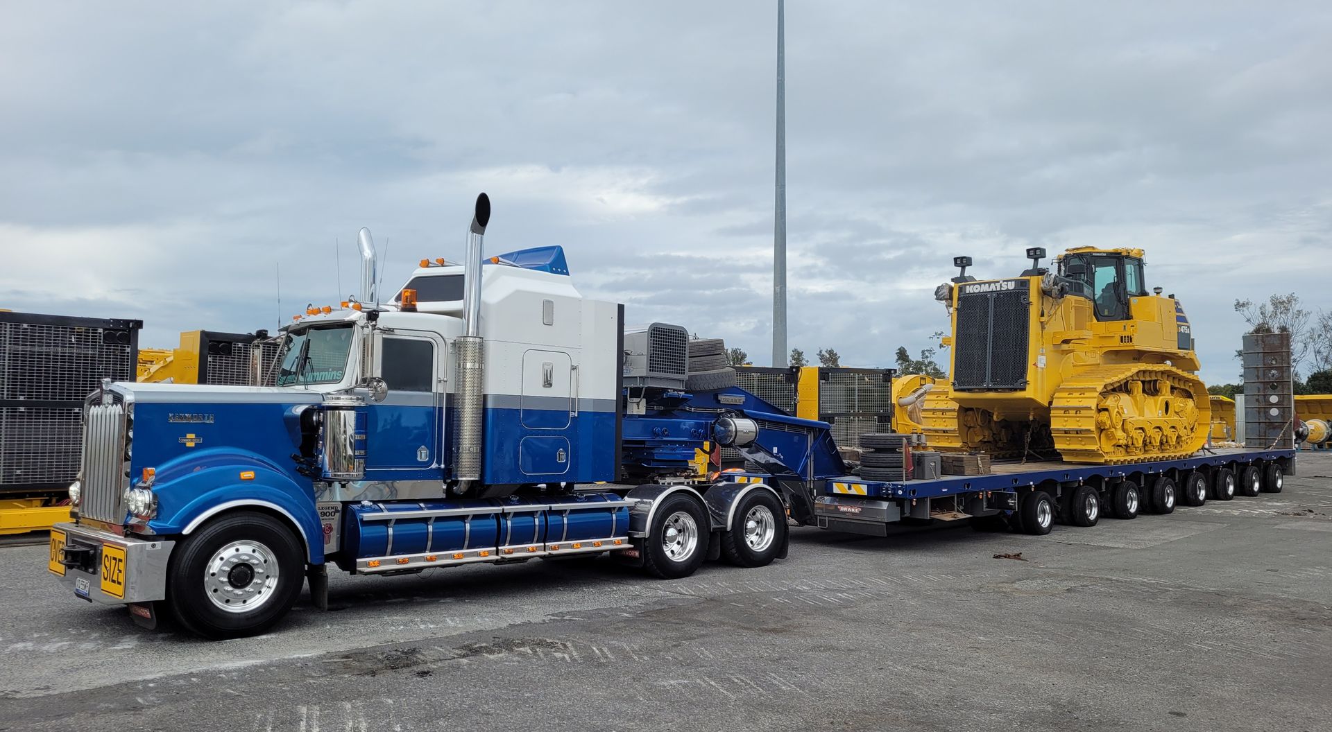 Blue and white semi-truck hauling a large yellow bulldozer on a trailer — ECC Heavy Haulage in Ormeau, QLD