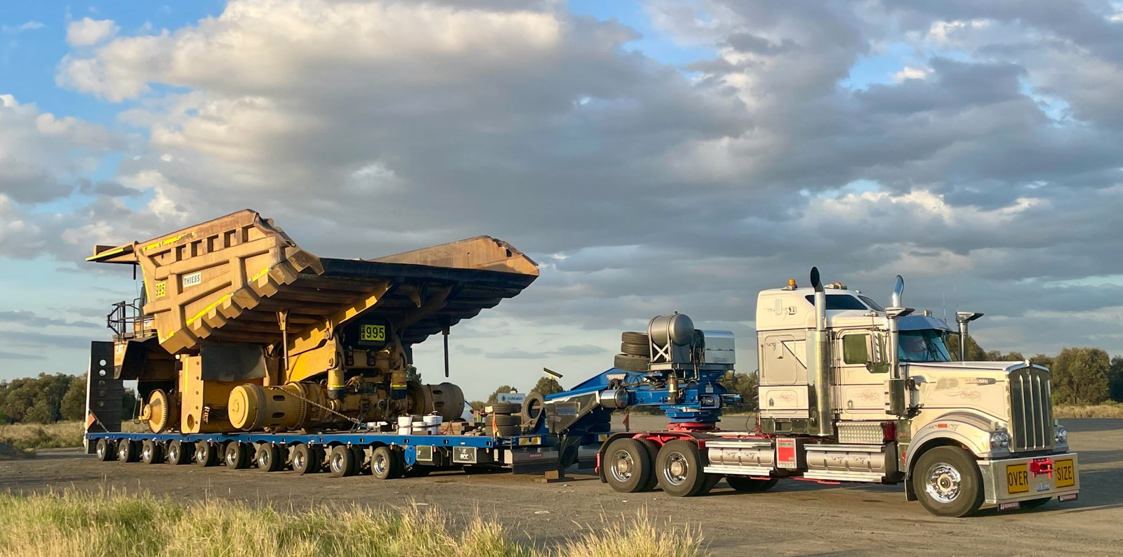 A large yellow earthmoving machine loaded on a transport trailer, being pulled by a semi-truck — ECC Heavy Haulage in Ormeau, QLD