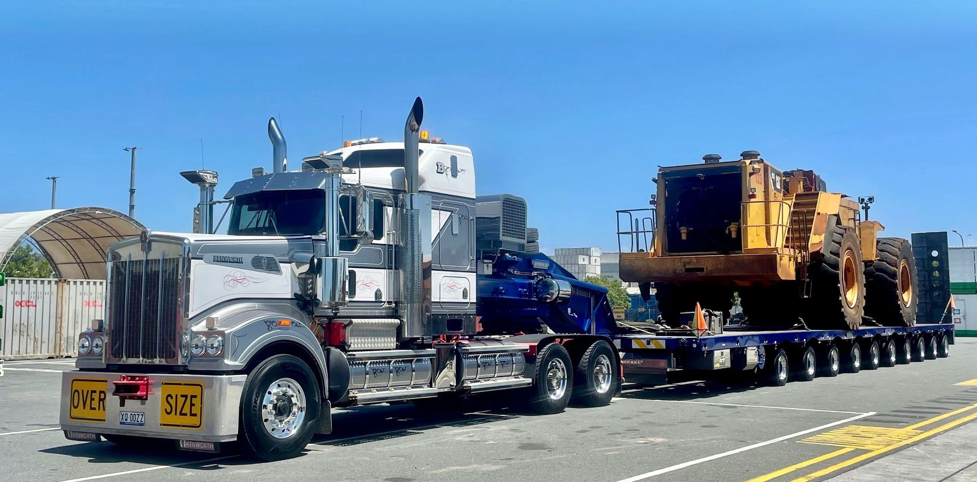 Truck hauling a large yellow earthmoving machine on a multi-axle trailer — ECC Heavy Haulage in Ormeau, QLD