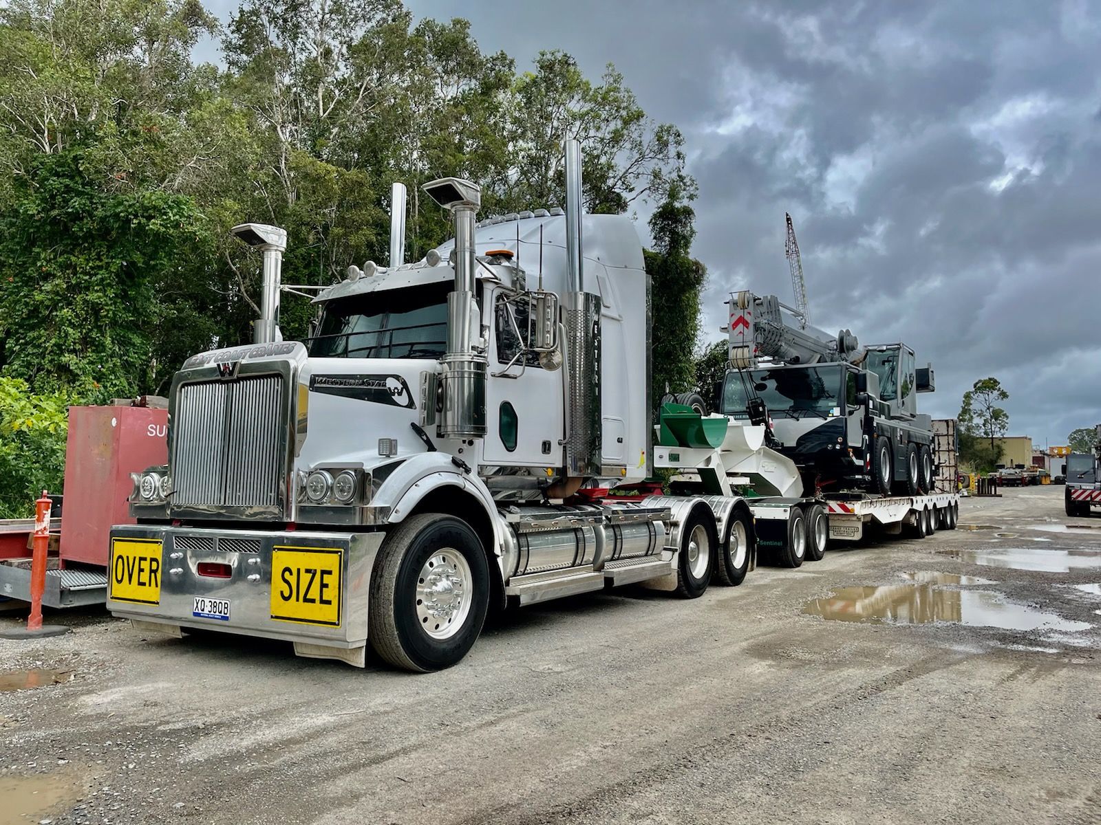 White semi-truck hauling a crane on a lowboy trailer on a muddy road — ECC Heavy Haulage in Ormeau, QLD