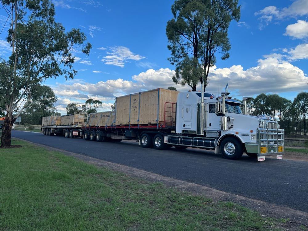 White Semi-truck Pulling Two Flatbed Trailers With Wooden Crates — ECC Heavy Haulage in Cairns, QLD