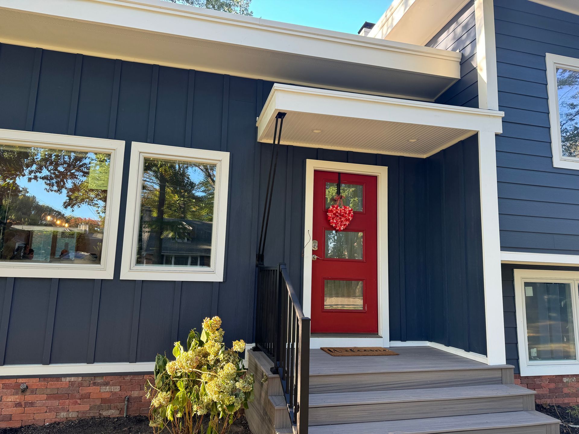 Blue house exterior with a red front door, white trim, and brick steps under a small awning