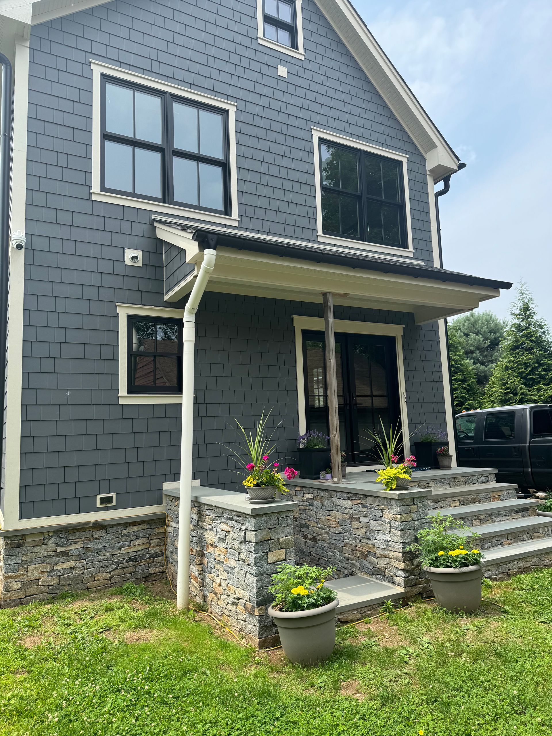Gray two-story house with stone porch, steps, and potted flowers in the front yard