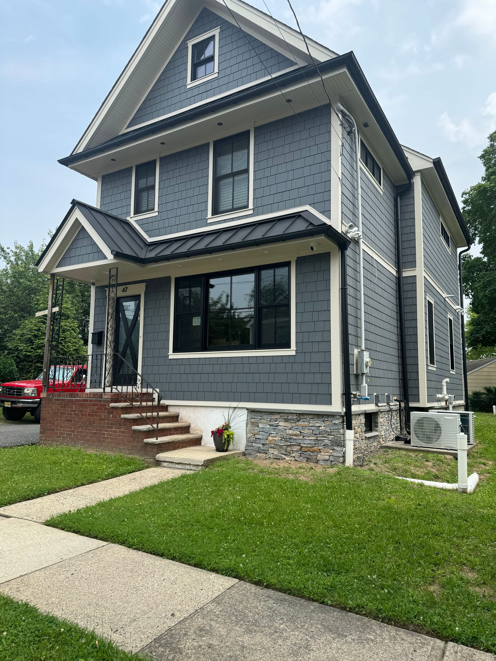 Gray two-story house with white trim, front steps, and a stone foundation beside a green lawn.