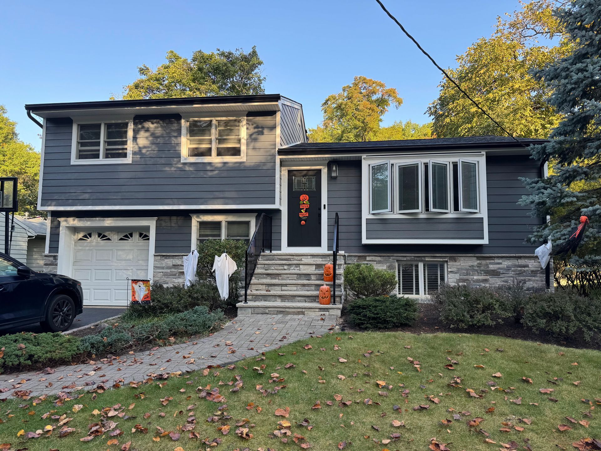 Gray two-story house with front steps, white trim, and autumn leaves on the lawn