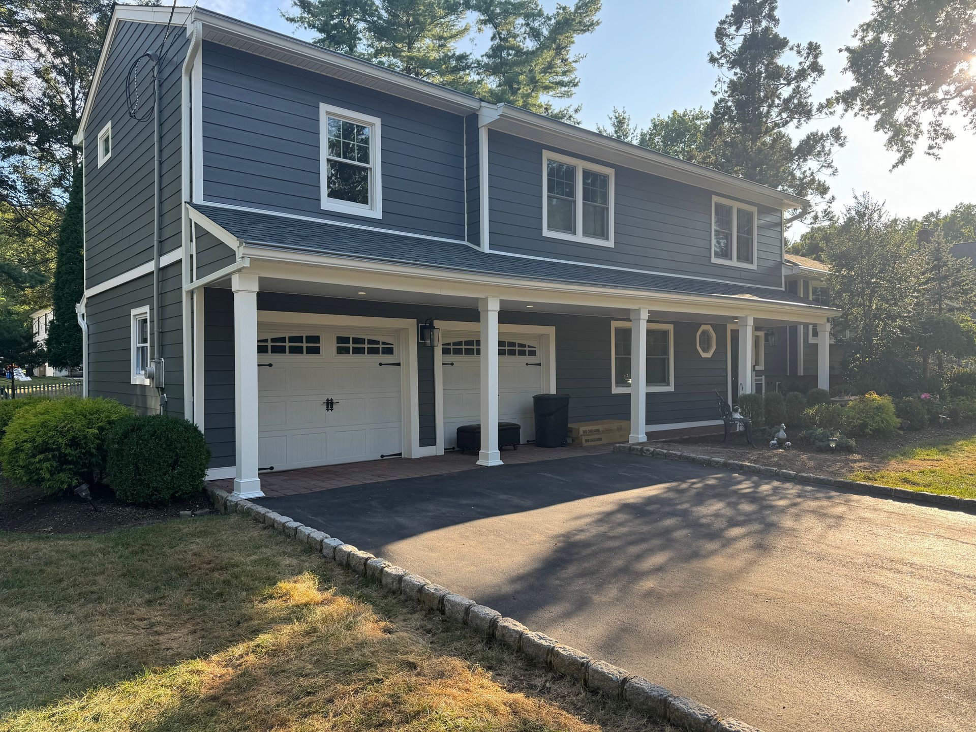 Two-story blue-gray house with white trim, front porch, and attached garage at the end of a driveway