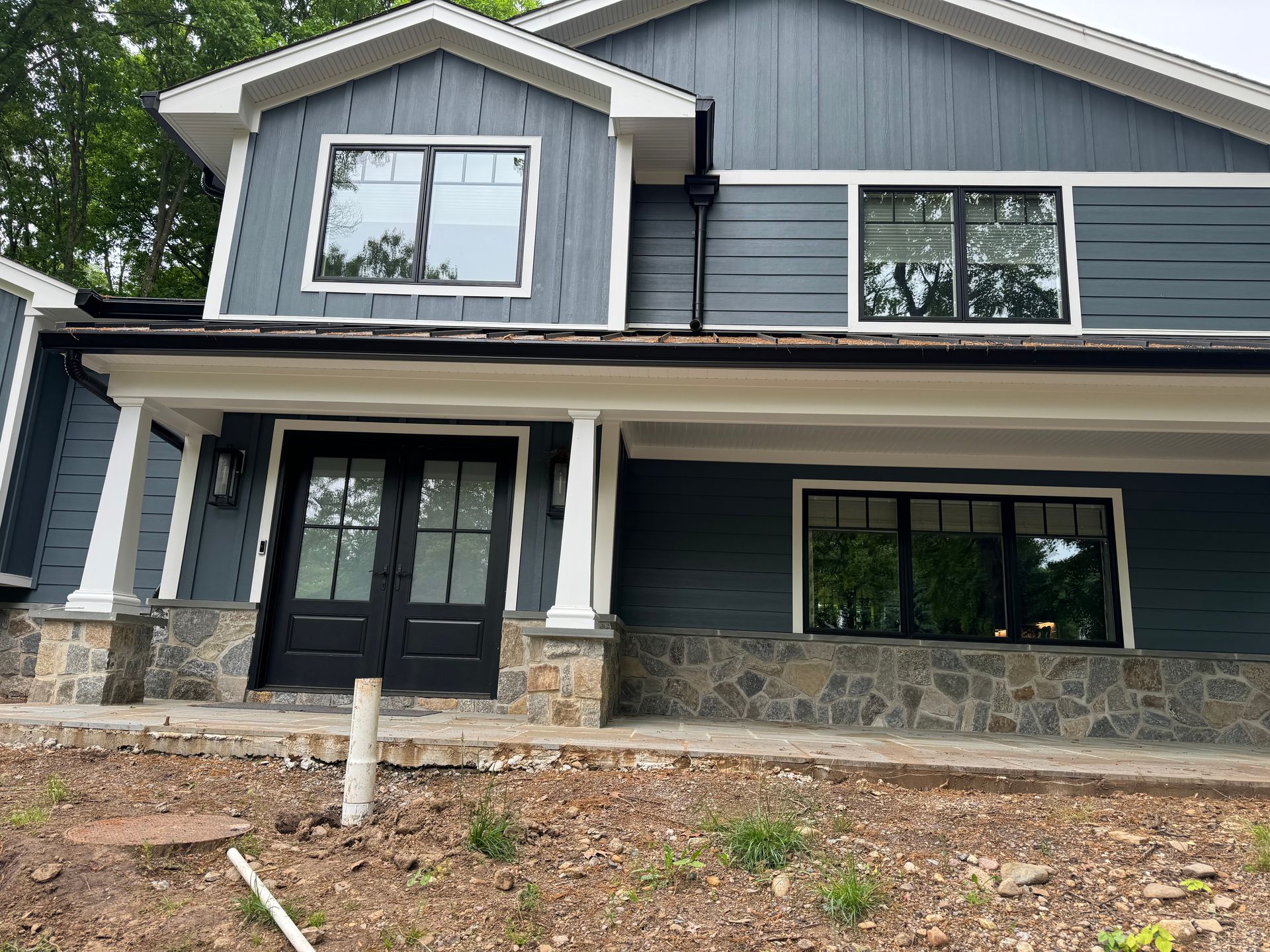 Modern gray house exterior with stone accents and large windows, viewed from the front yard.