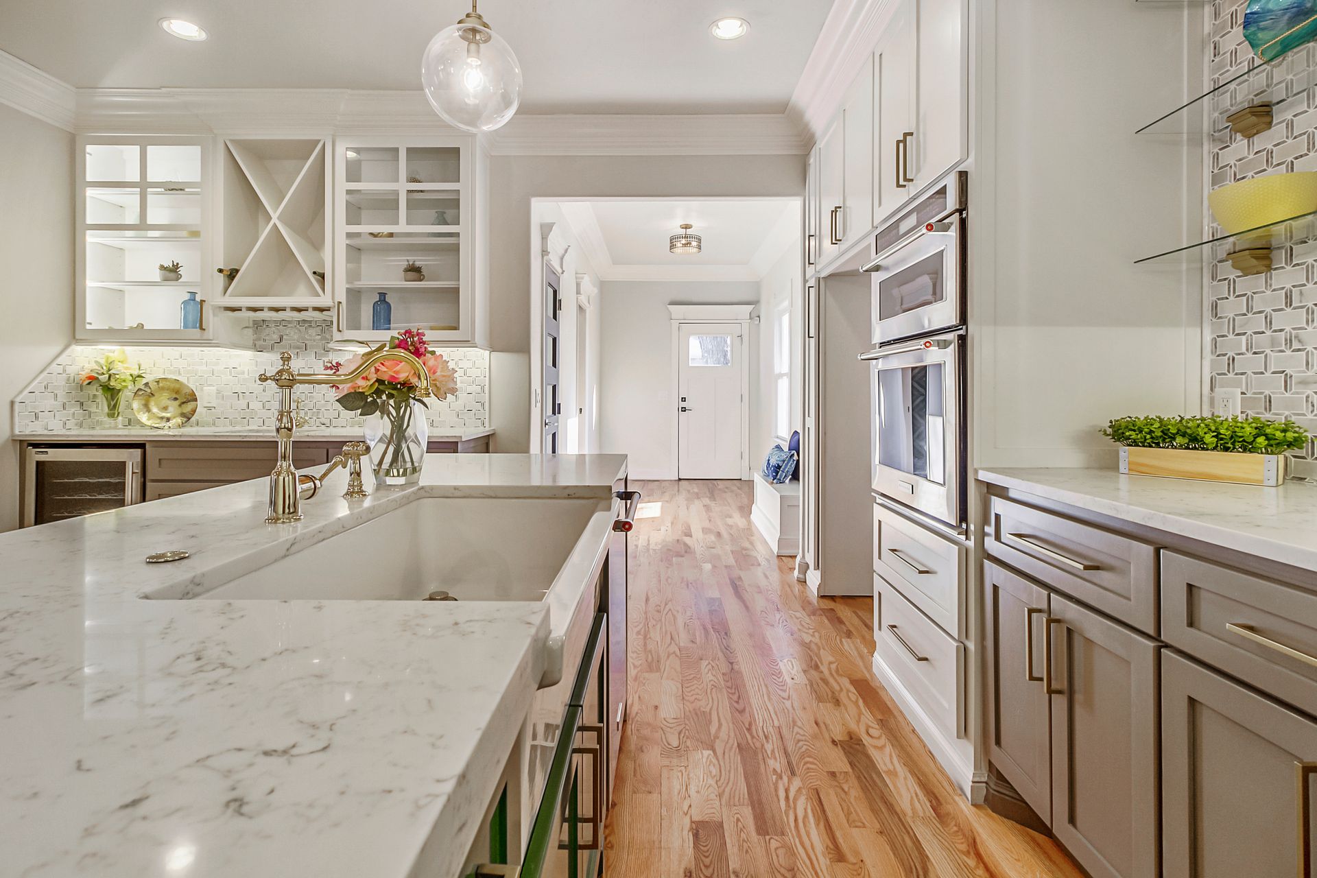 Modern kitchen with white cabinets, marble countertops, and wooden floors.