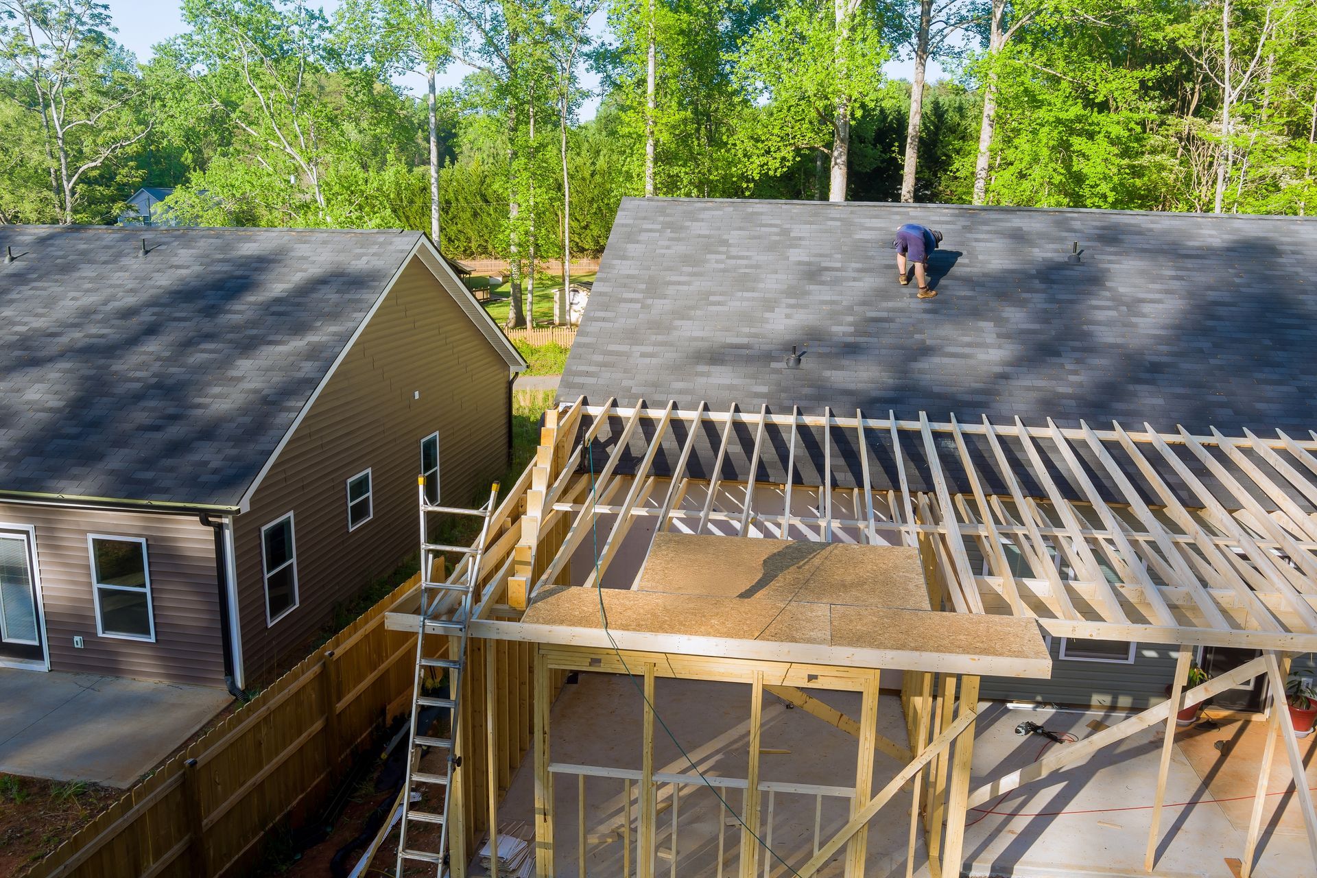 Two houses under roof repair, with exposed rafters and a worker on the right roof