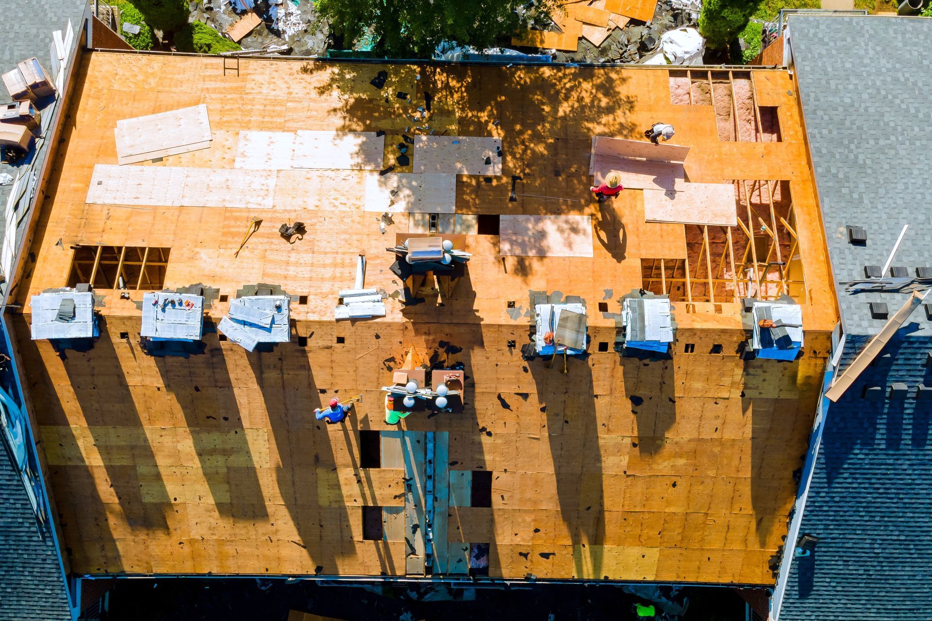 Overhead view of a building roof under construction with workers, tools, and materials in sunlight