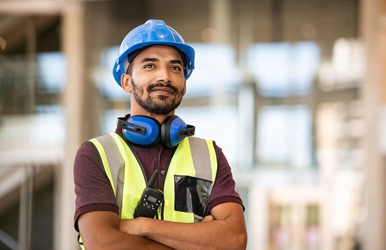 Construction worker in a hard hat and safety vest using a tablet at a building site.
