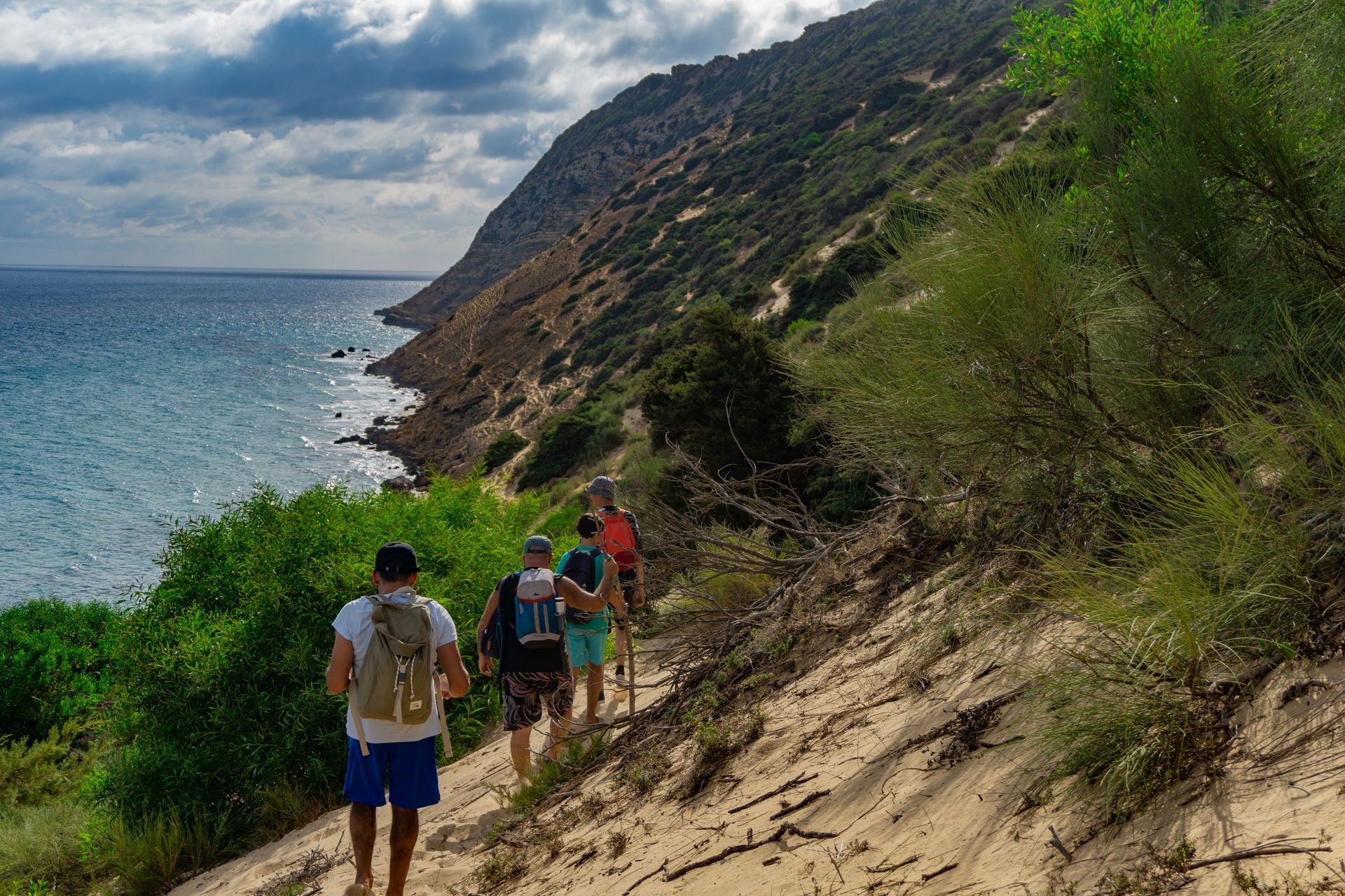Hikers walking along a sandy coastal trail beside cliffs and the ocean