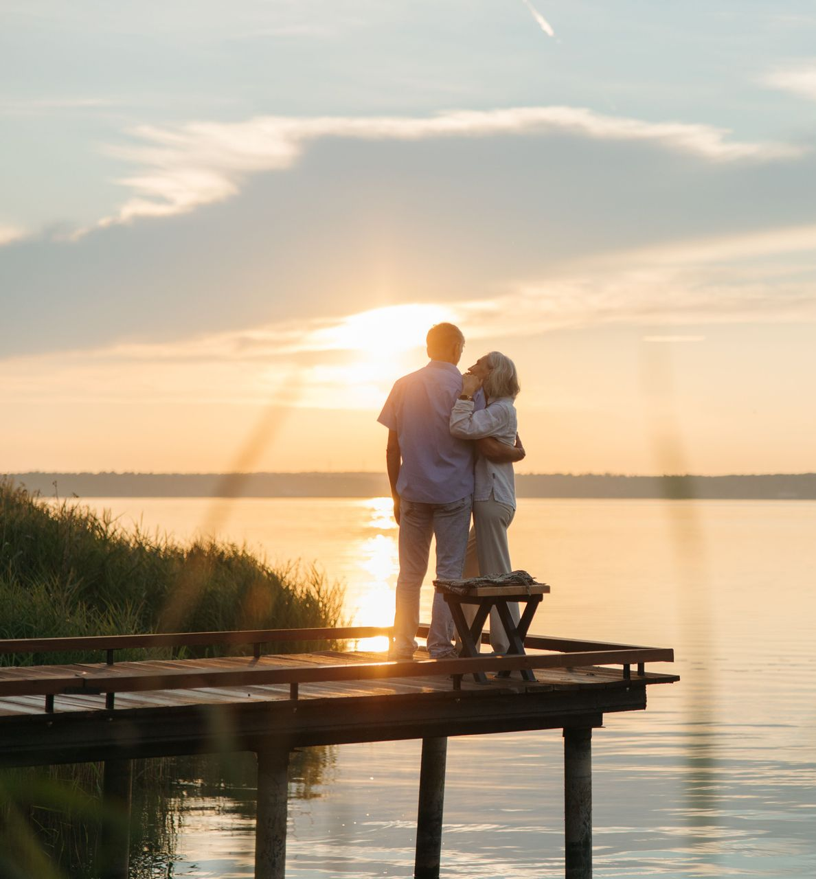 Two people standing on a wooden dock at sunset by a calm lake