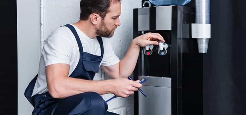 Plumber in gray overalls inspecting a water heater with a wrench in a utility room
