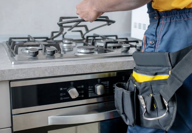 Person installing a gas stove burner in a modern kitchen, with tools clipped to a utility belt