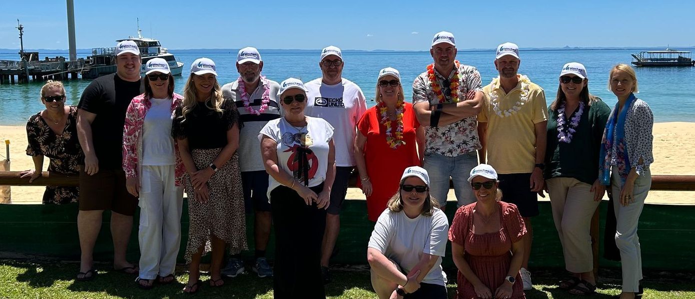 Group of people wearing matching hats posing together by the beach with boats and ocean in the background