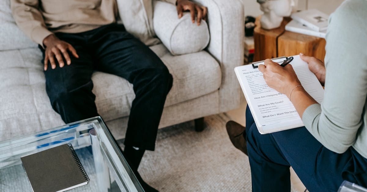 Person taking notes on a clipboard during a counselling or consultation session with a seated client