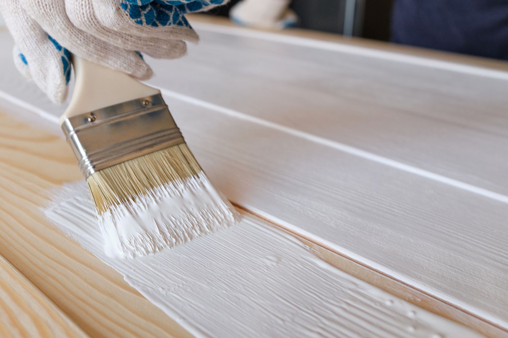 Gloved hand painting white paint onto wooden planks with a paintbrush.