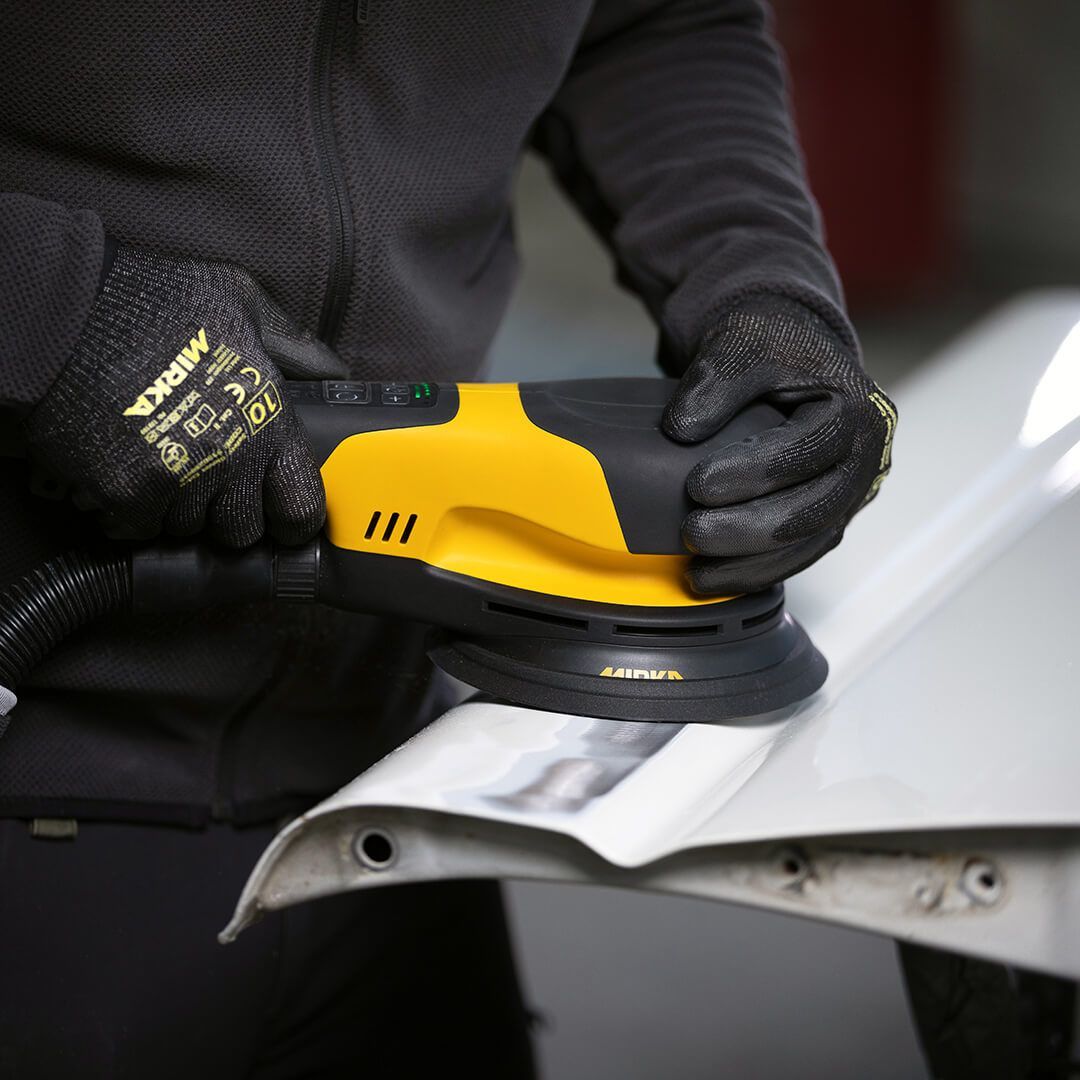 Person using a yellow power sander on a car body panel