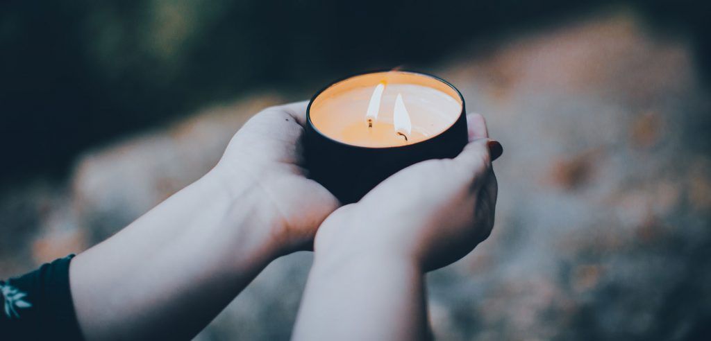Hands cupping a lit candle, the warm glow contrasting against the blurred, dark background.