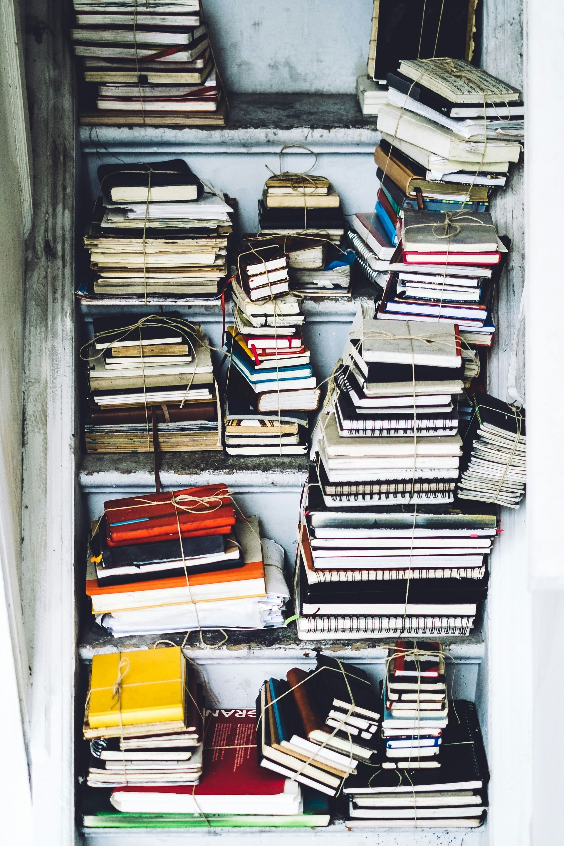 Tracy Manu Blog - Tall stacks of various journals and notebooks piled neatly on each step of a light-colored staircase.