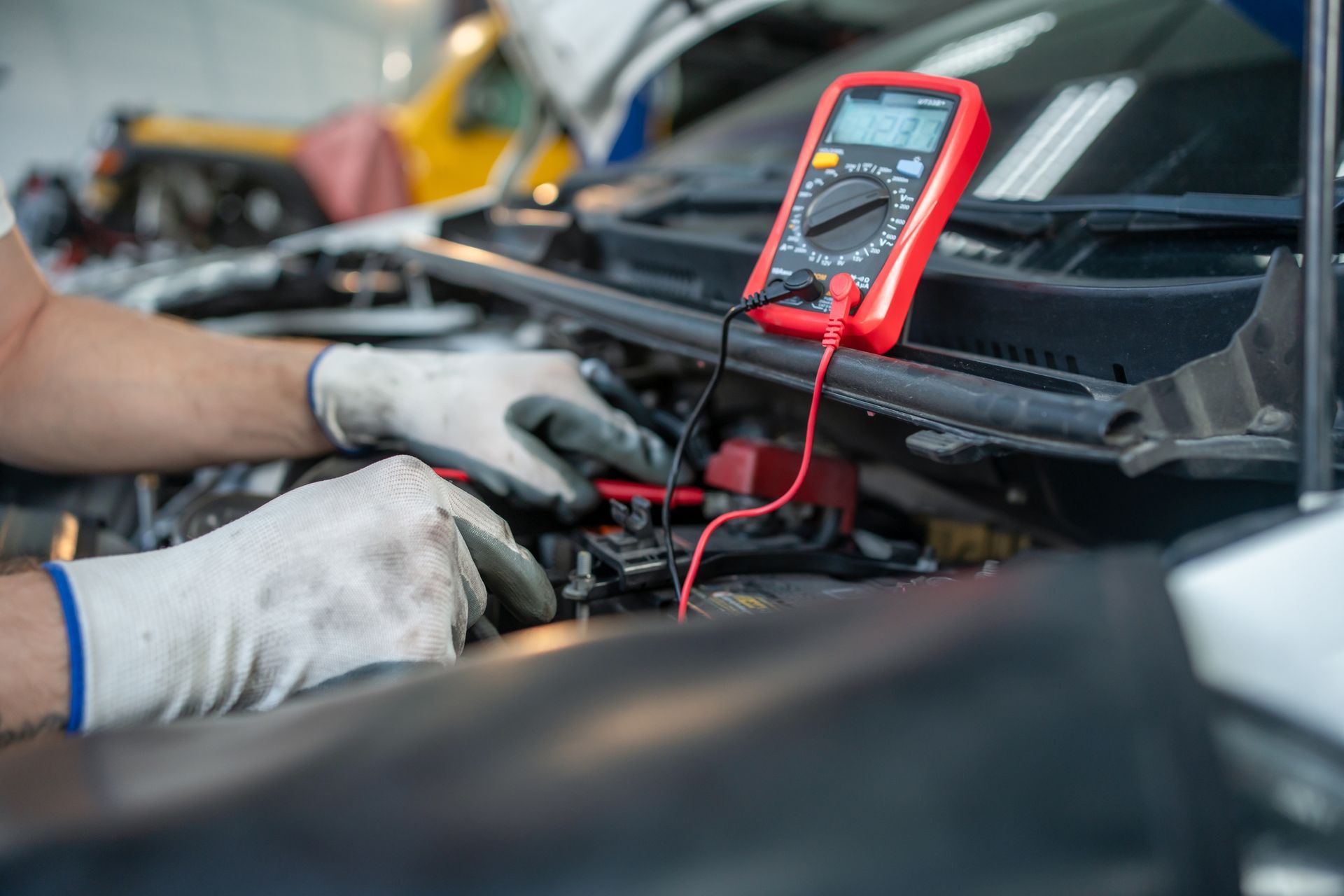 A person is working on a car with a multimeter.