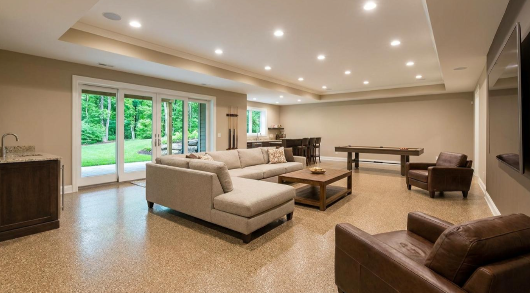 Spacious modern living room with beige sofas, recessed lighting, and sliding glass doors to a green patio