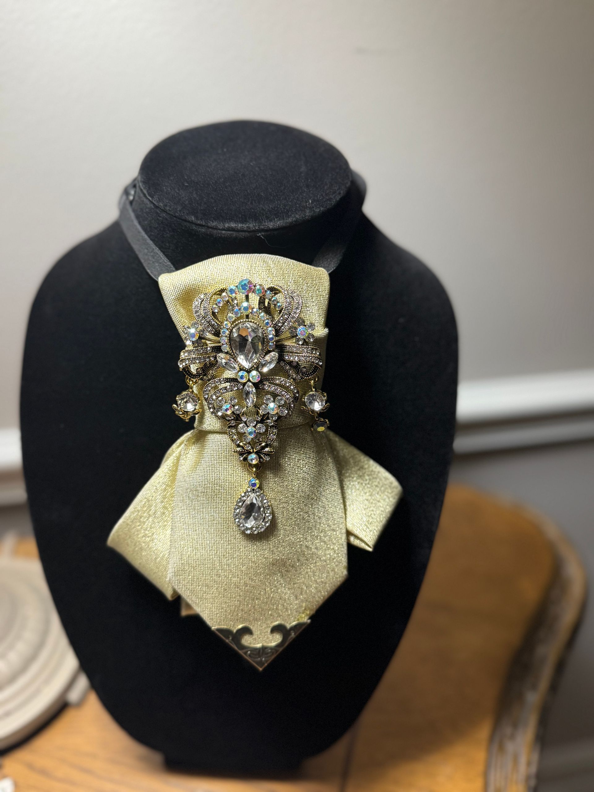 Black velvet jewelry bust displaying a gold bow tie brooch with a sparkling crystal centerpiece and pendant