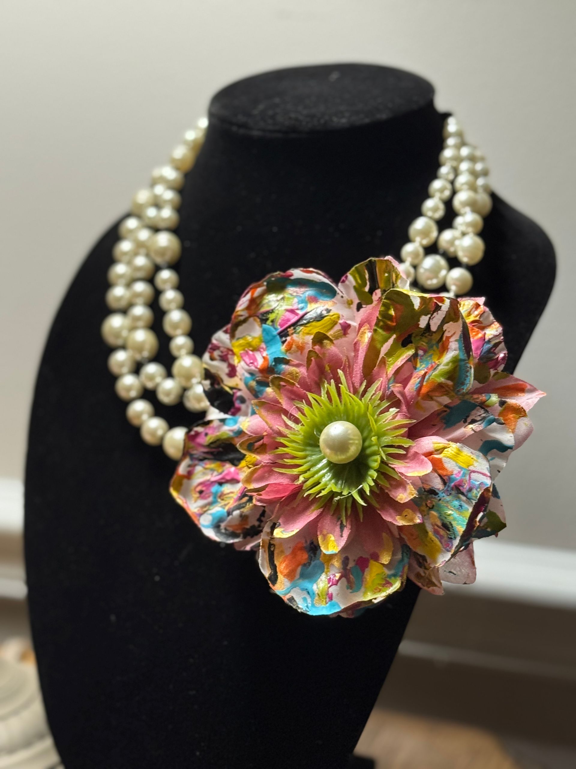Pearl necklace with a large colorful floral brooch on a black display bust