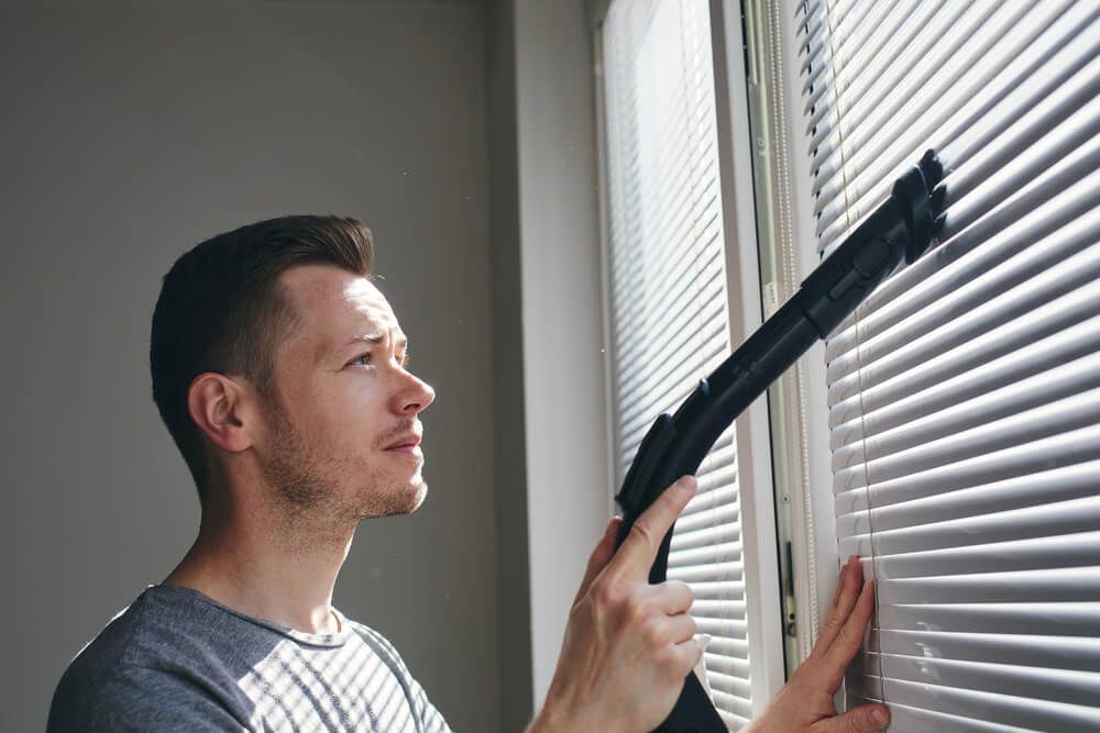 A Man is Cleaning a Window With a Vacuum Cleaner — Wow Clean Cairns in Bayview Heights, QLD