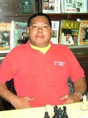 A man in a red shirt is sitting at a table with chess pieces