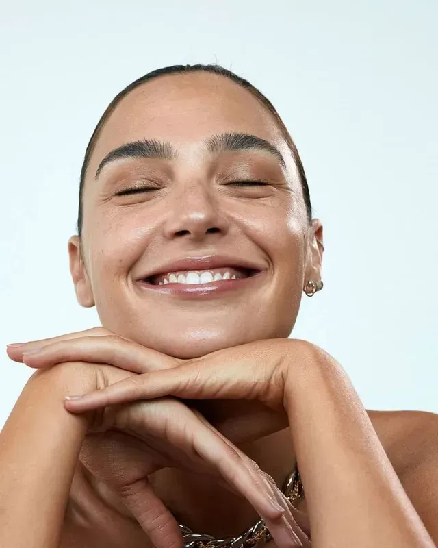 Smiling person resting chin on folded hands against a light blue background