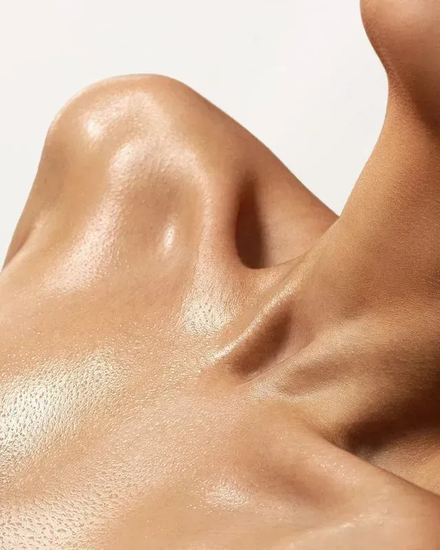 Close-up of a glossy, tan human shoulder and neck in soft lighting
