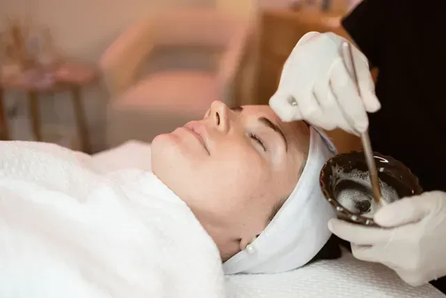 Client receiving a scalp treatment while lying on a spa bed, with gloved hands applying product to the hairline