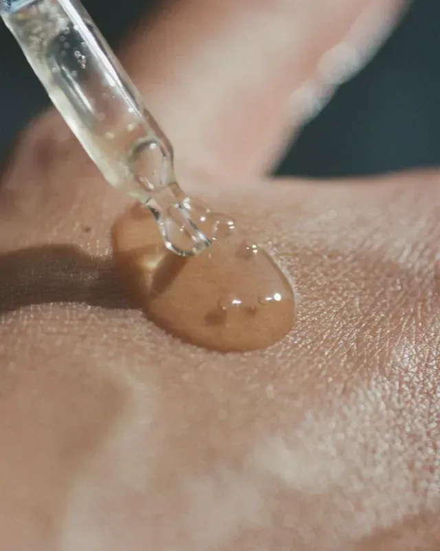 Dropper applying beige serum onto skin close-up