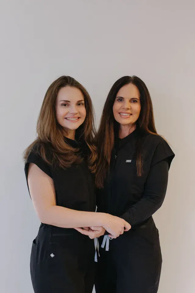 Two people in black outfits standing together and smiling against a plain light background