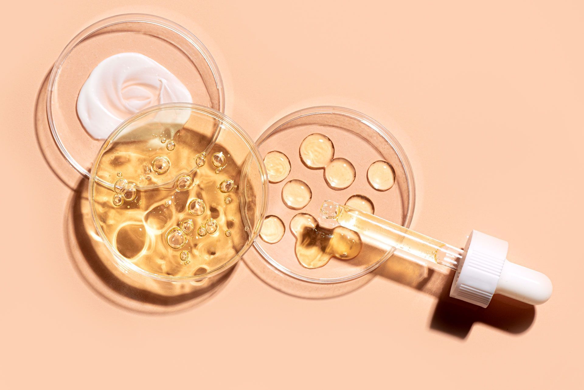 Open cosmetic jar with golden serum and white dropper on peach background