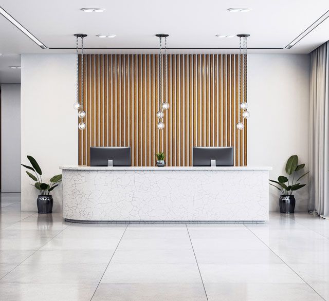 Modern minimalist reception desk with white counter, wood slat wall, and potted plants in a bright lobby