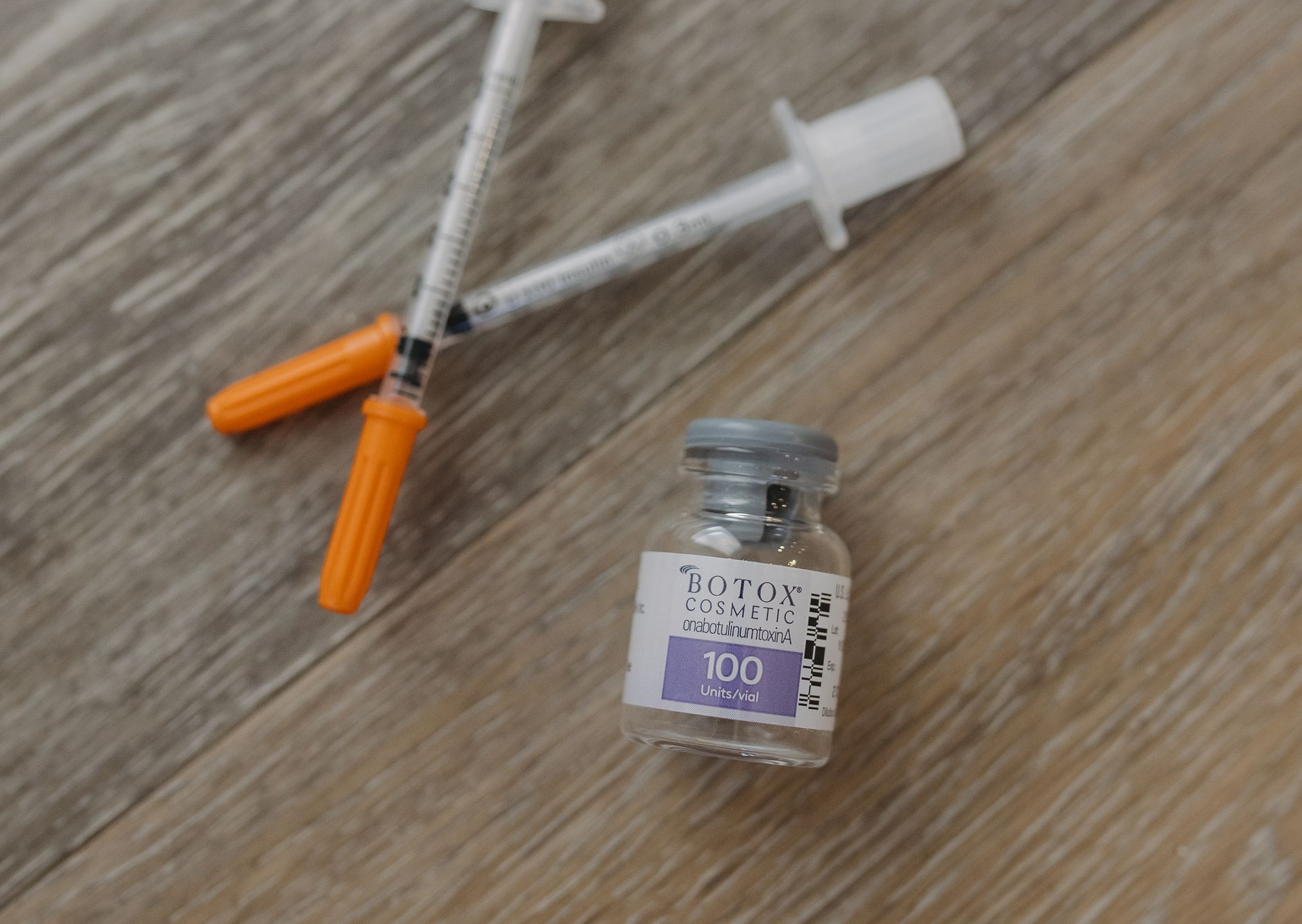 Syringe with orange caps beside a small glass medicine vial on a wooden surface