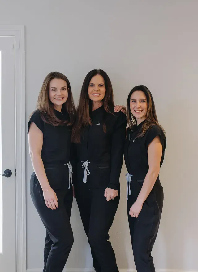 Three women in black outfits standing together against a light gray wall