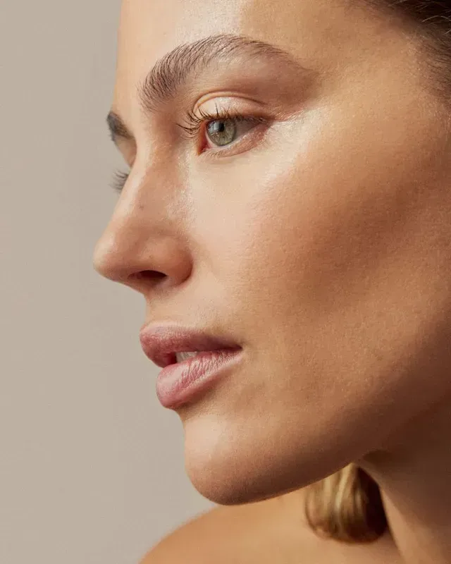 Side-profile portrait of a person with smooth skin and neutral makeup against a beige background