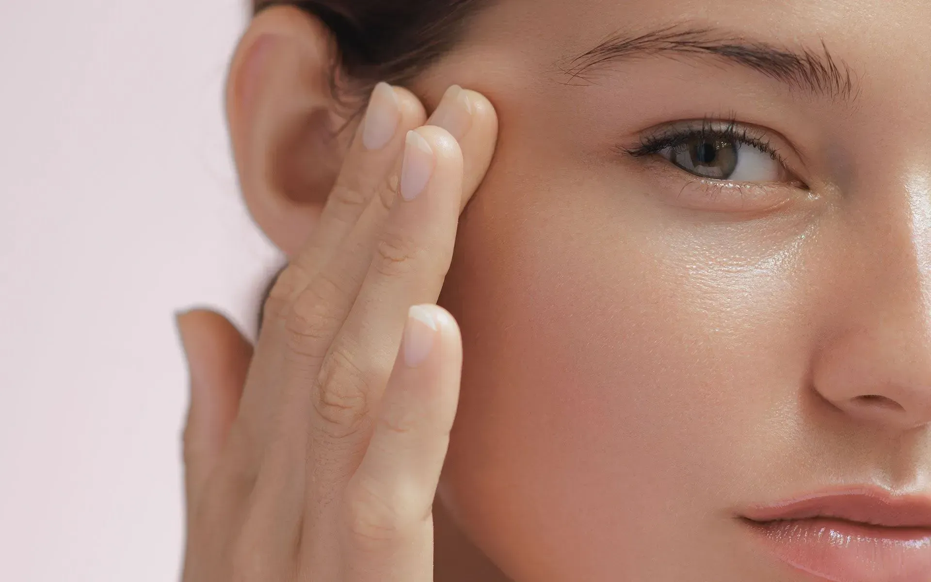 Close-up of a person applying skincare cream to their cheek with a hand