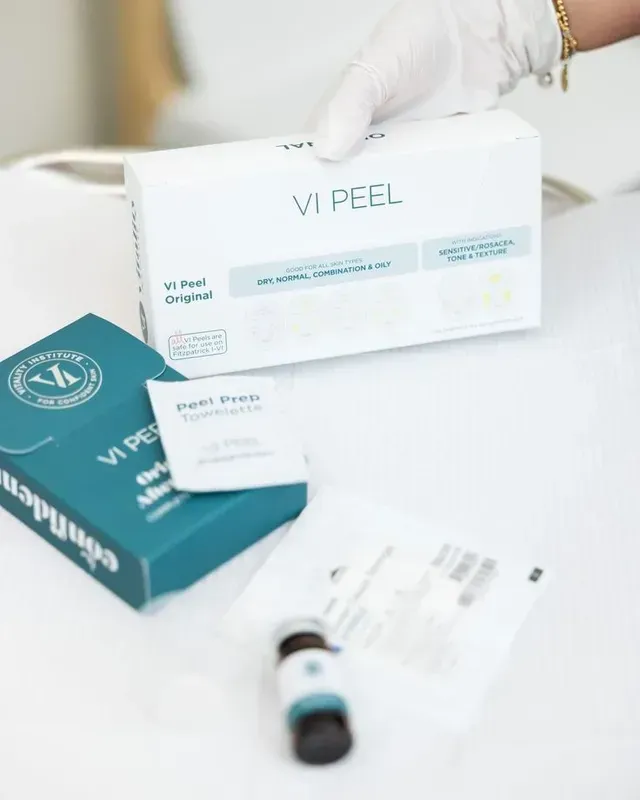 Gloved hand holding a VI PEEL skincare box with product packaging and vial on a white surface