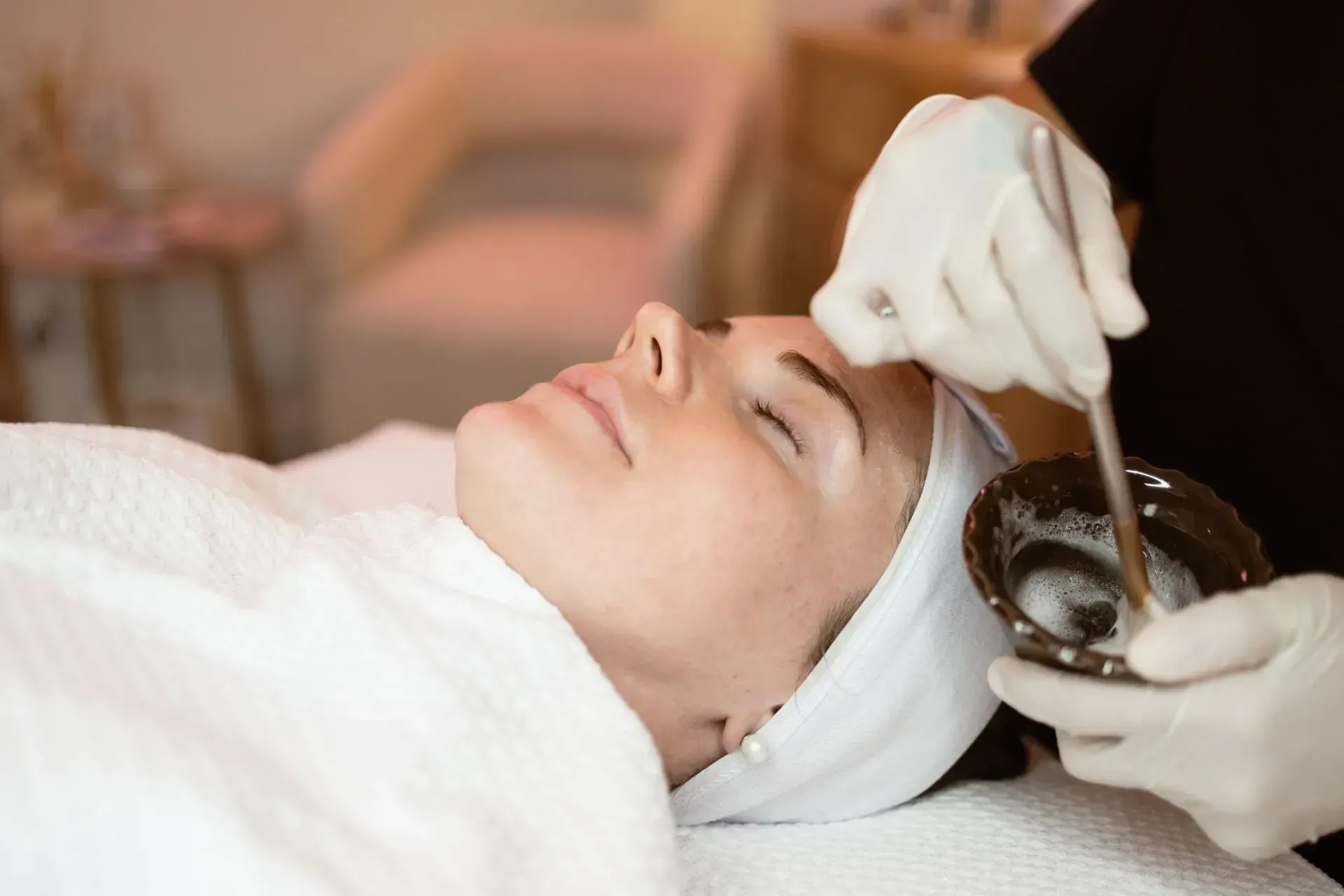 Person receiving a facial treatment while a gloved hand applies cream near the forehead