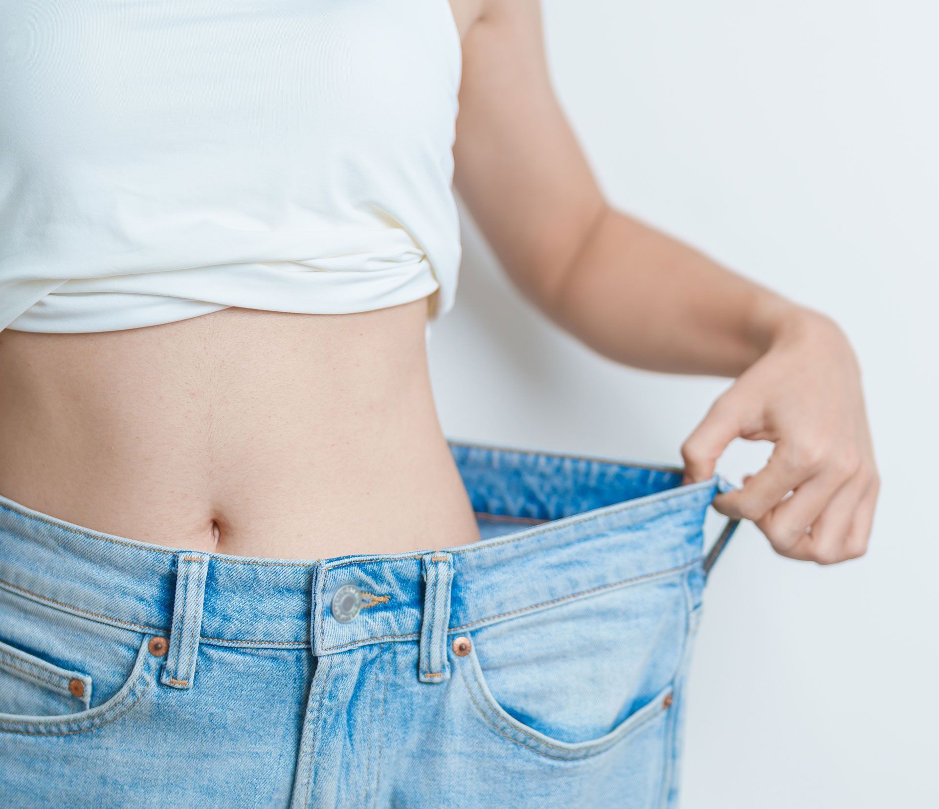 Person holding loose blue jeans at the waist, showing a slimmed waistline