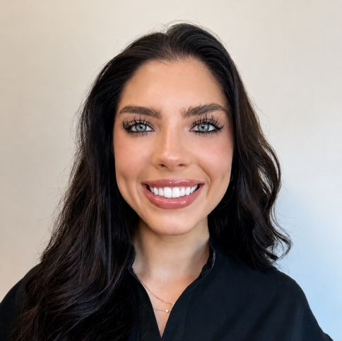 Smiling woman with dark hair against a light background, wearing a black top