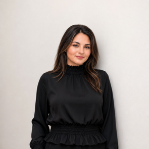 Woman in a black blouse standing against a plain light background.