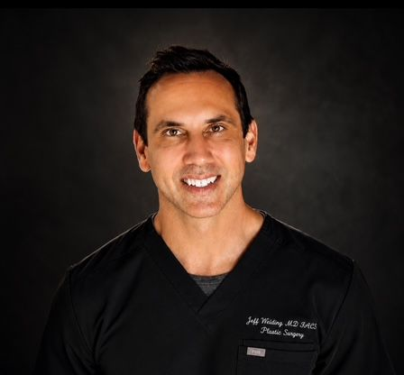 Smiling man in black medical scrubs against a dark background