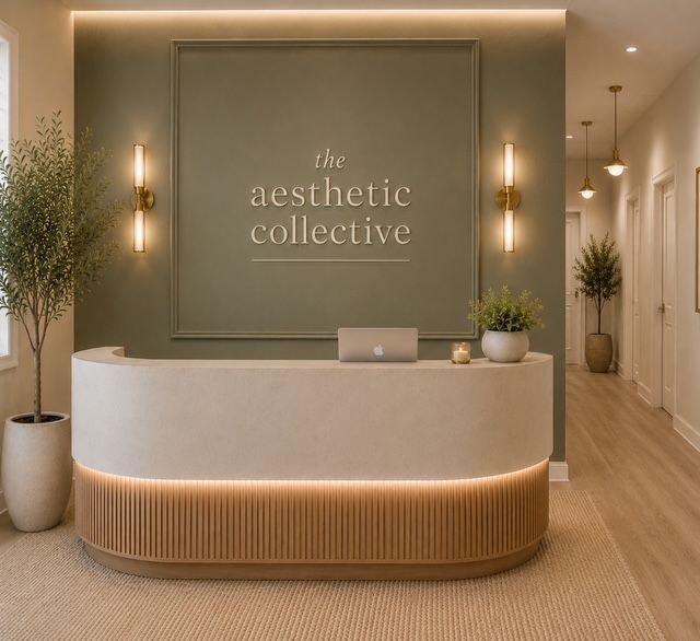 Modern spa reception desk with sage wall, warm lighting, and “the aesthetic collective” sign