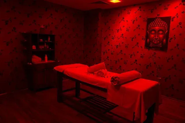 Red-lit massage room with treatment table, folded towels, shelf, and wall art